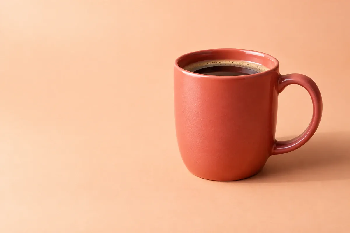 A coral-red coffee cup sits on the right with open space on the left; side lighting casts a shadow behind it to the right
